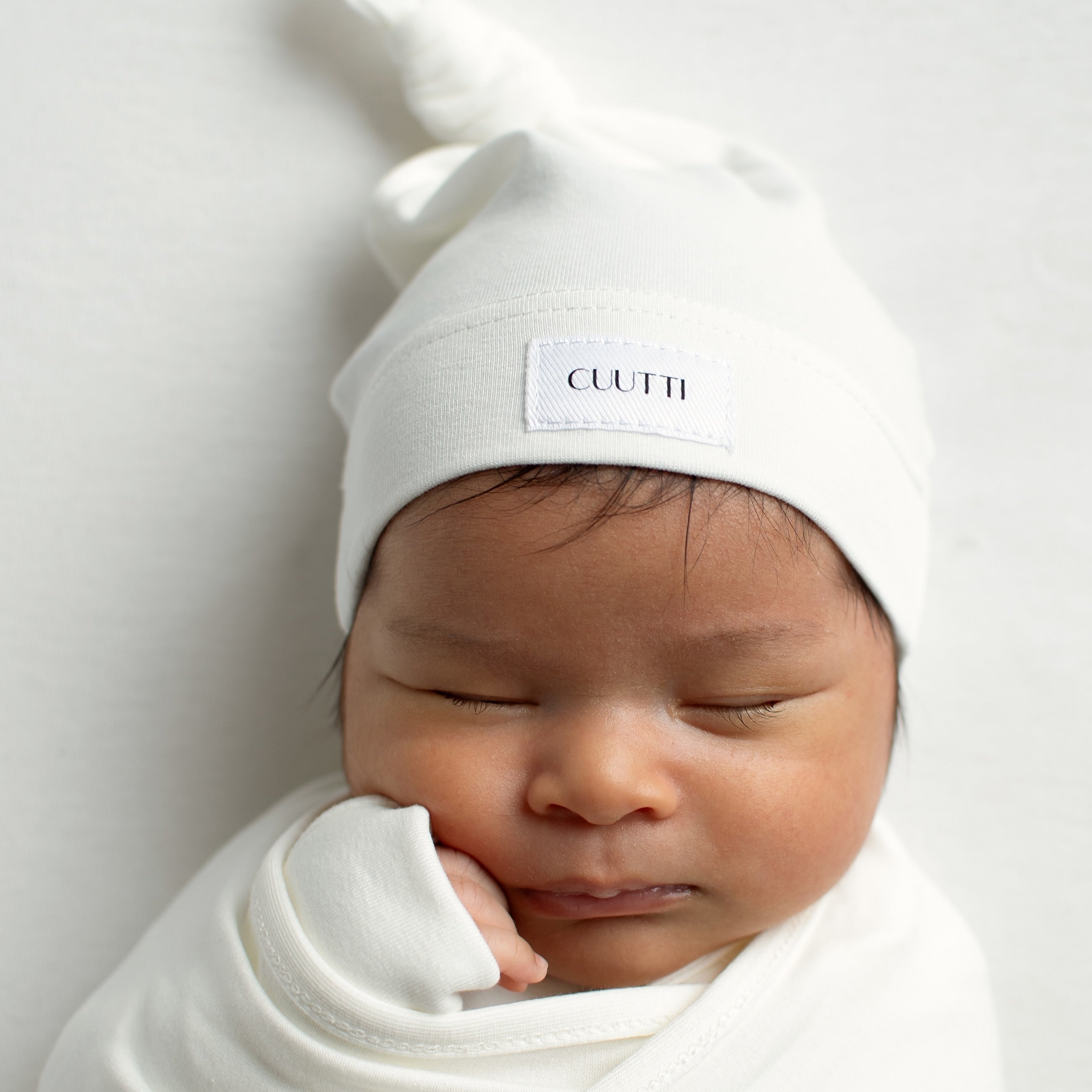 Close-up of a 1-month-old baby boy wrapped in an ivory CUUTTI baby swaddle.