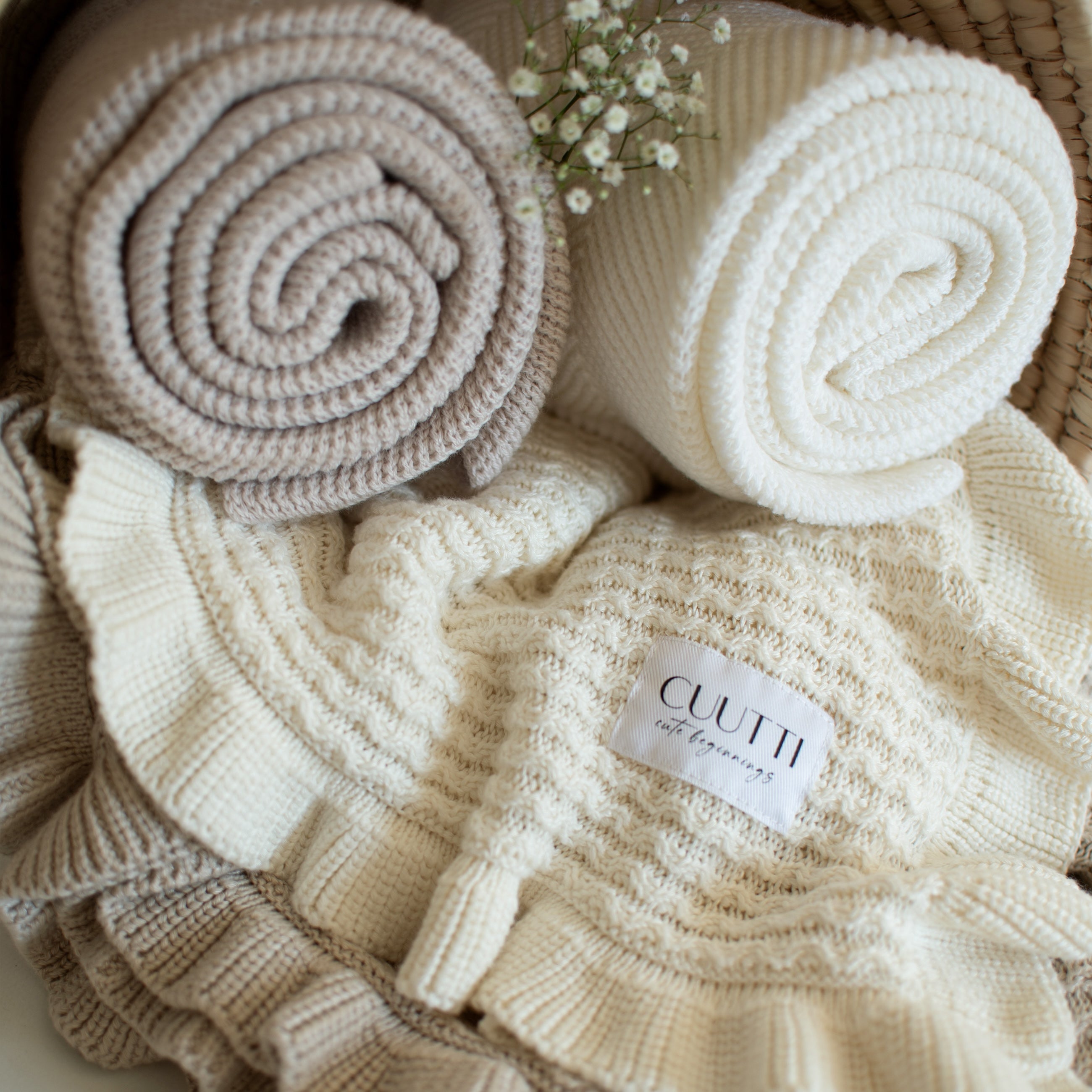 Close-up of four CUUTTI blankets in a small basket, featuring ivory and beige Ballerina bamboo blankets at the bottom.