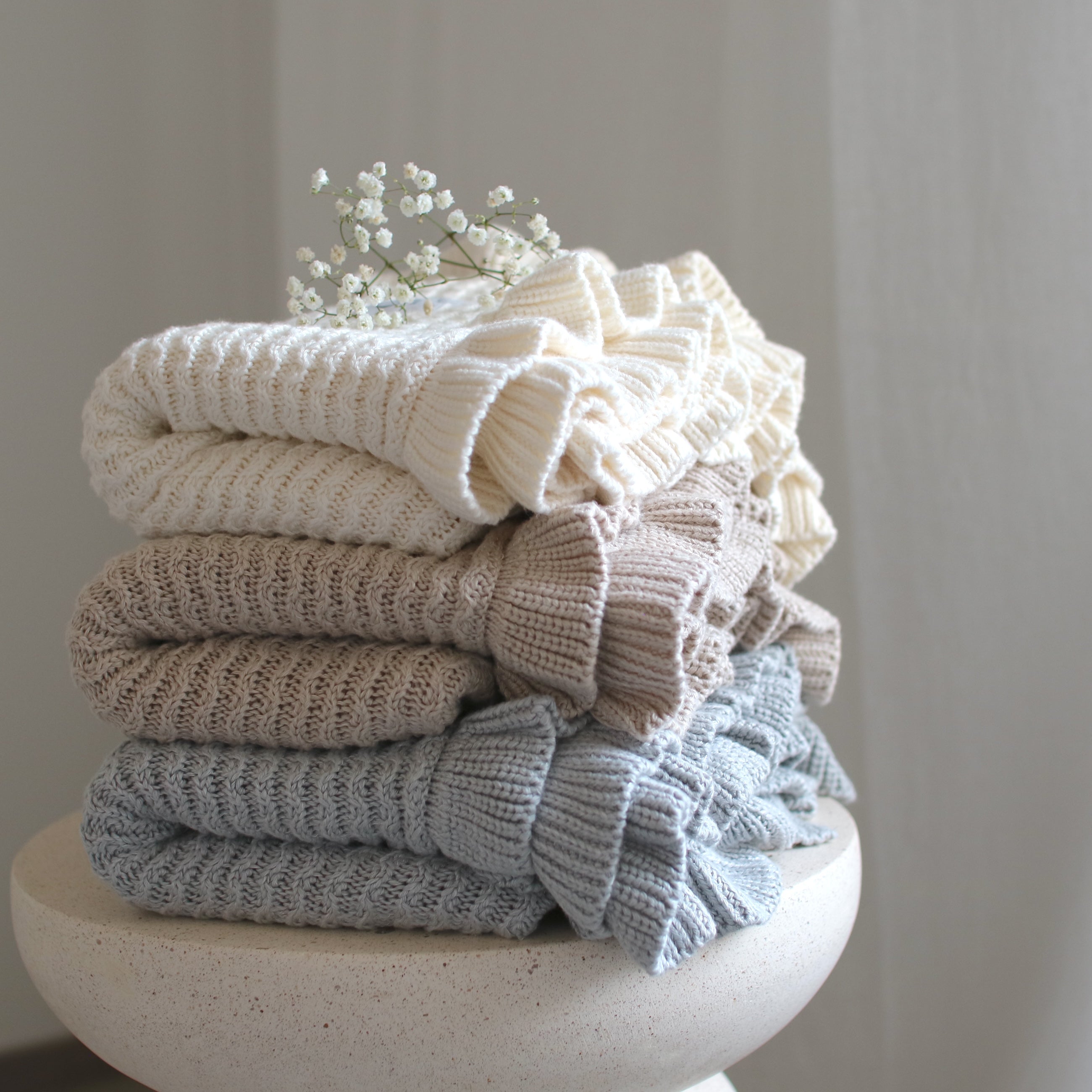 Three CUUTTI Ballerina bamboo blankets in ivory, beige, and cloud color neatly folded on a small table.