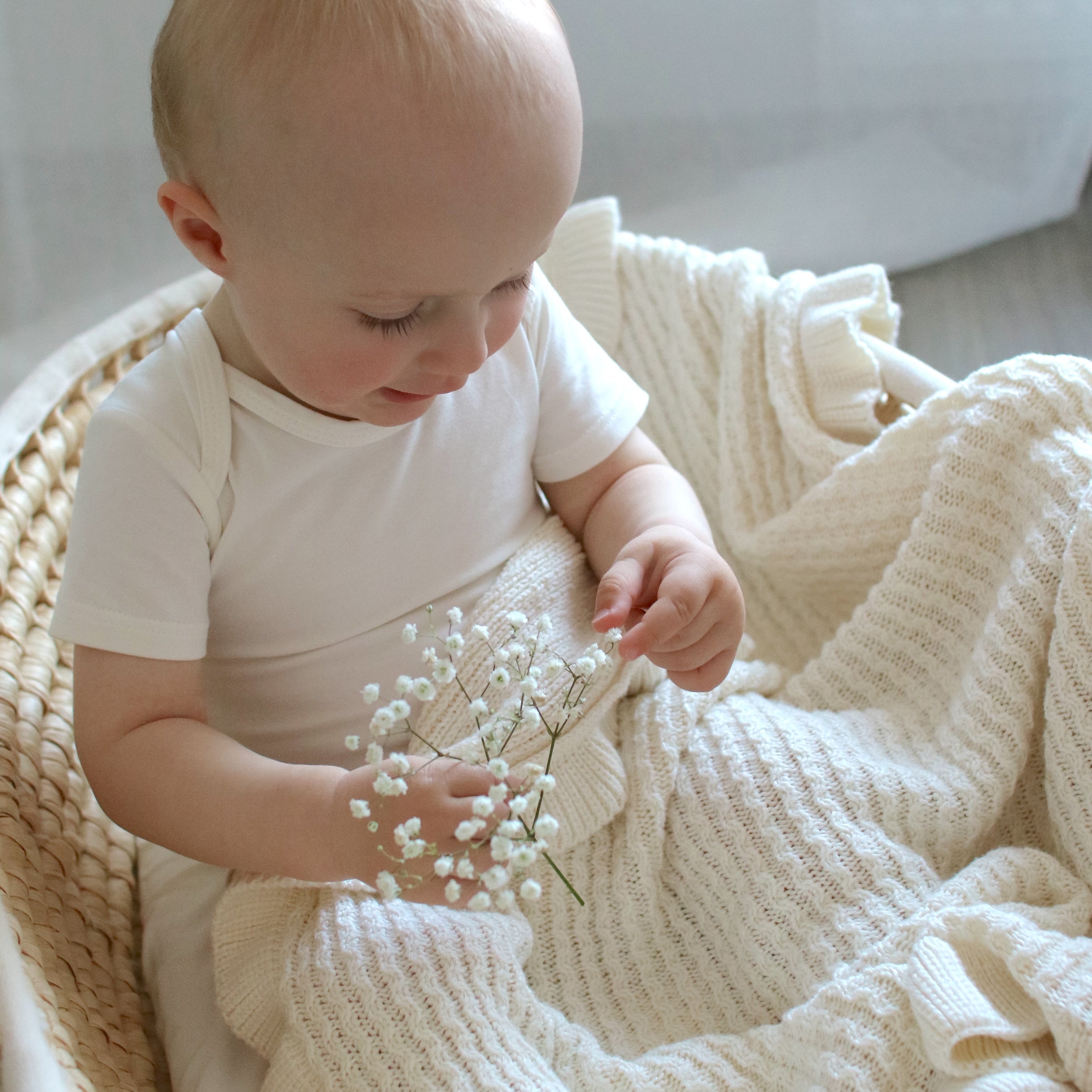 Little boy sitting in a basket, covering himself with an ivory CUUTTI Ballerina bamboo blanket to keep warm and cozy.