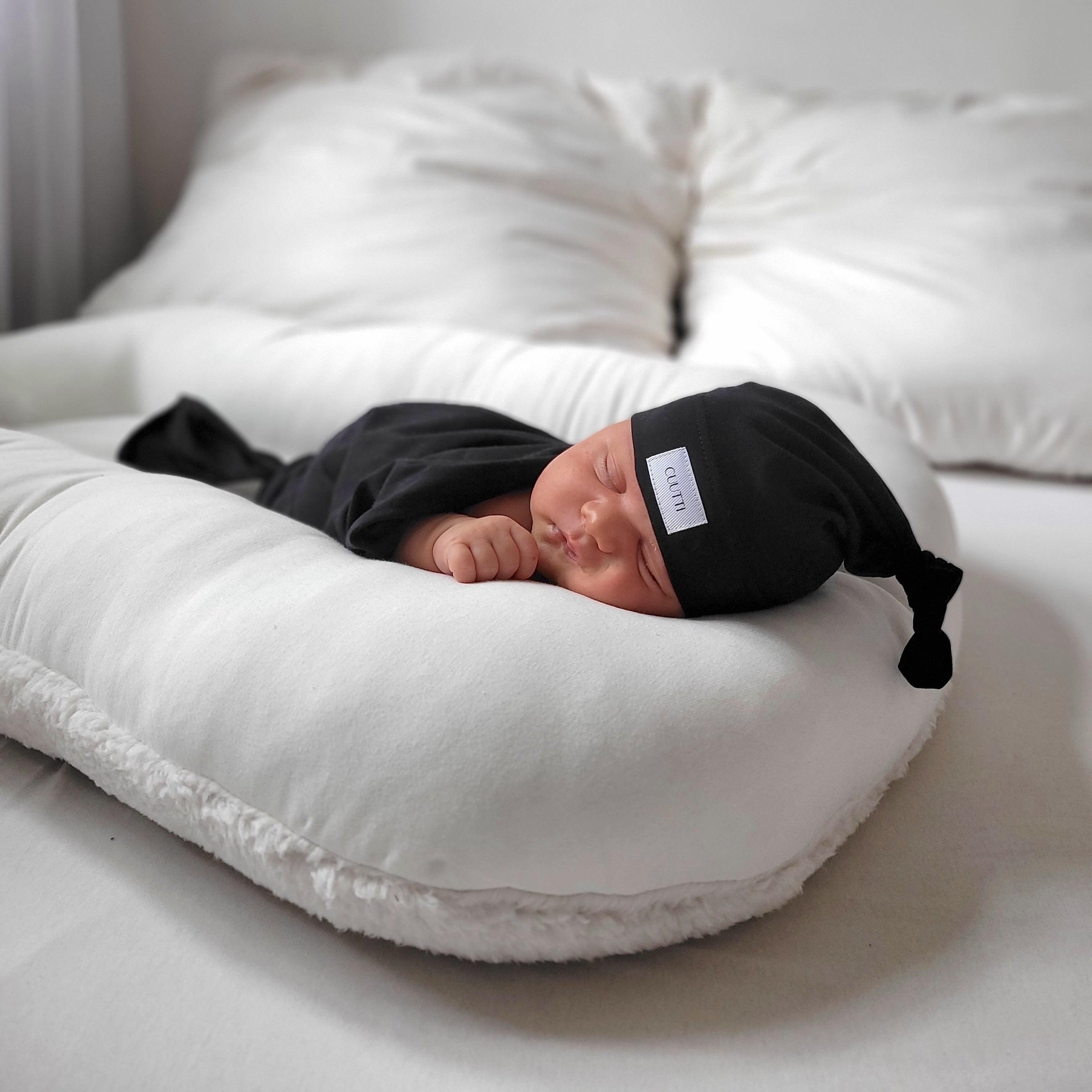 Newborn baby boy sleeping peacefully, wearing a black CUUTTI baby beanie.