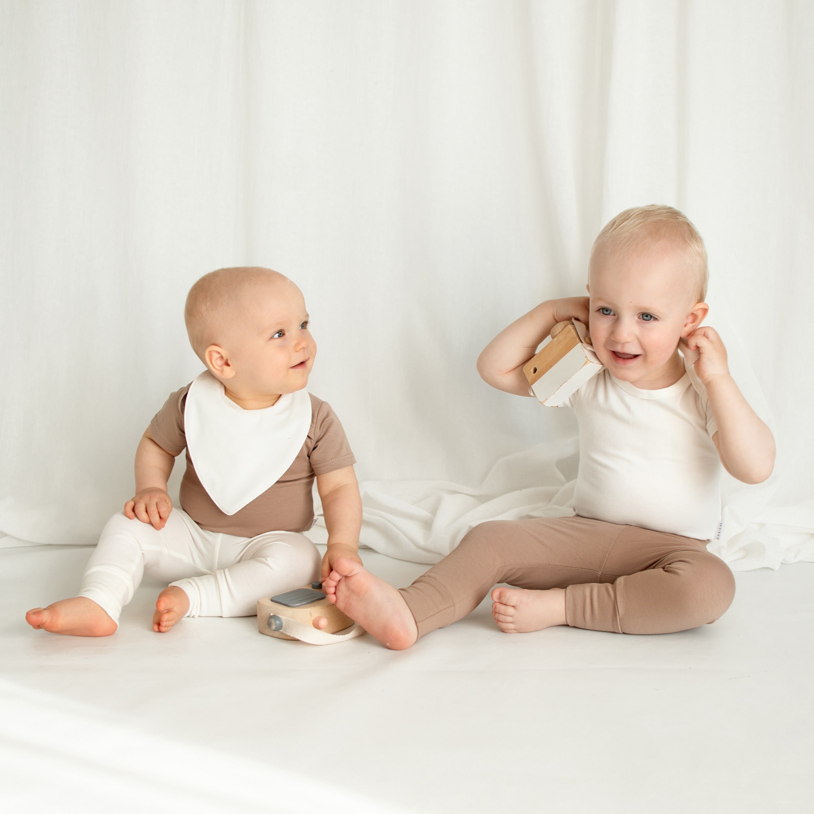 A little girl and boy sitting together on the floor, wearing stylish CUUTTI outfits: the girl in ivory leggings and the boy in cookie-colored leggings.