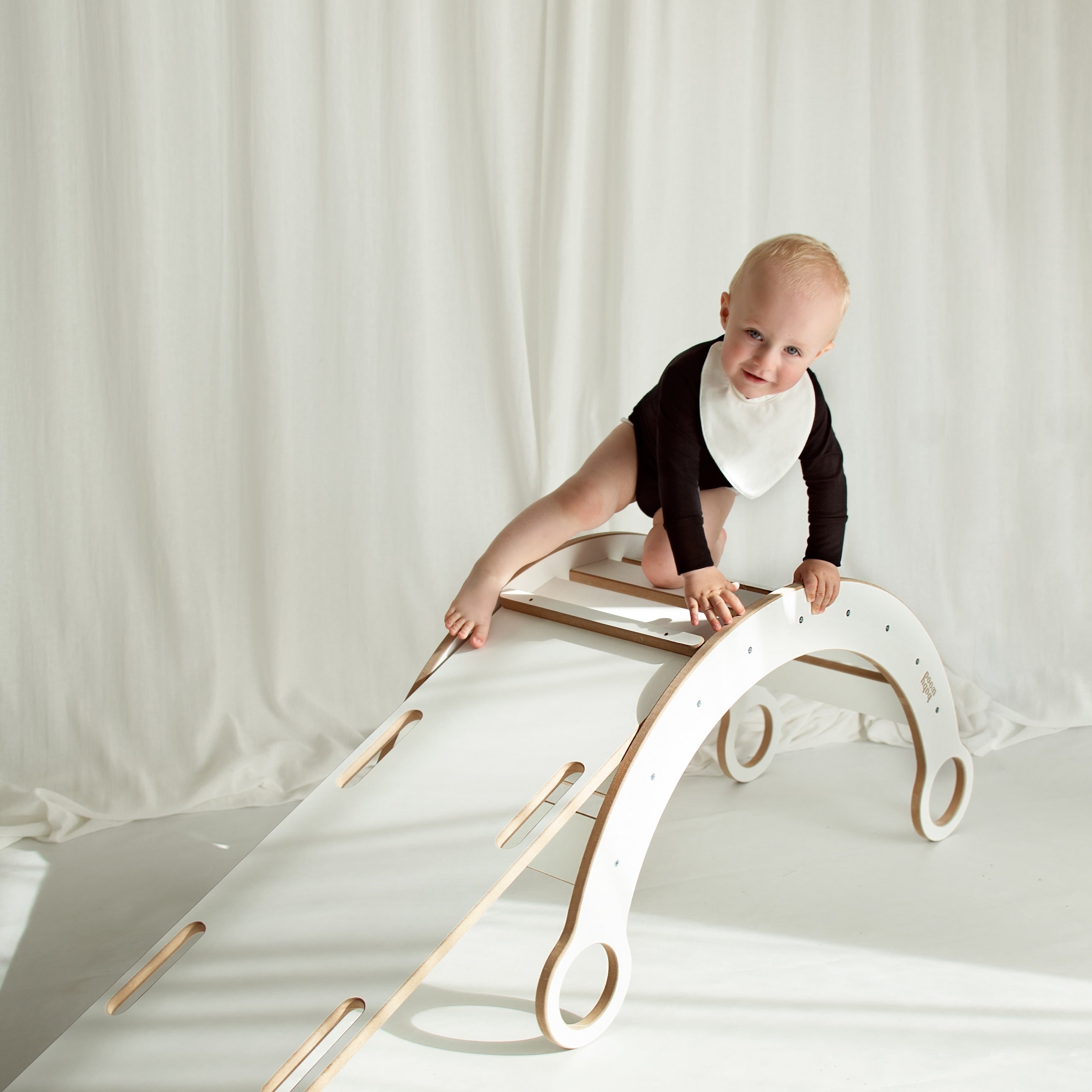 Little boy playing on a climbing arch, wearing a stylish CUUTTI outfit with a black long sleeve bodysuit and an ivory waterproof bib.