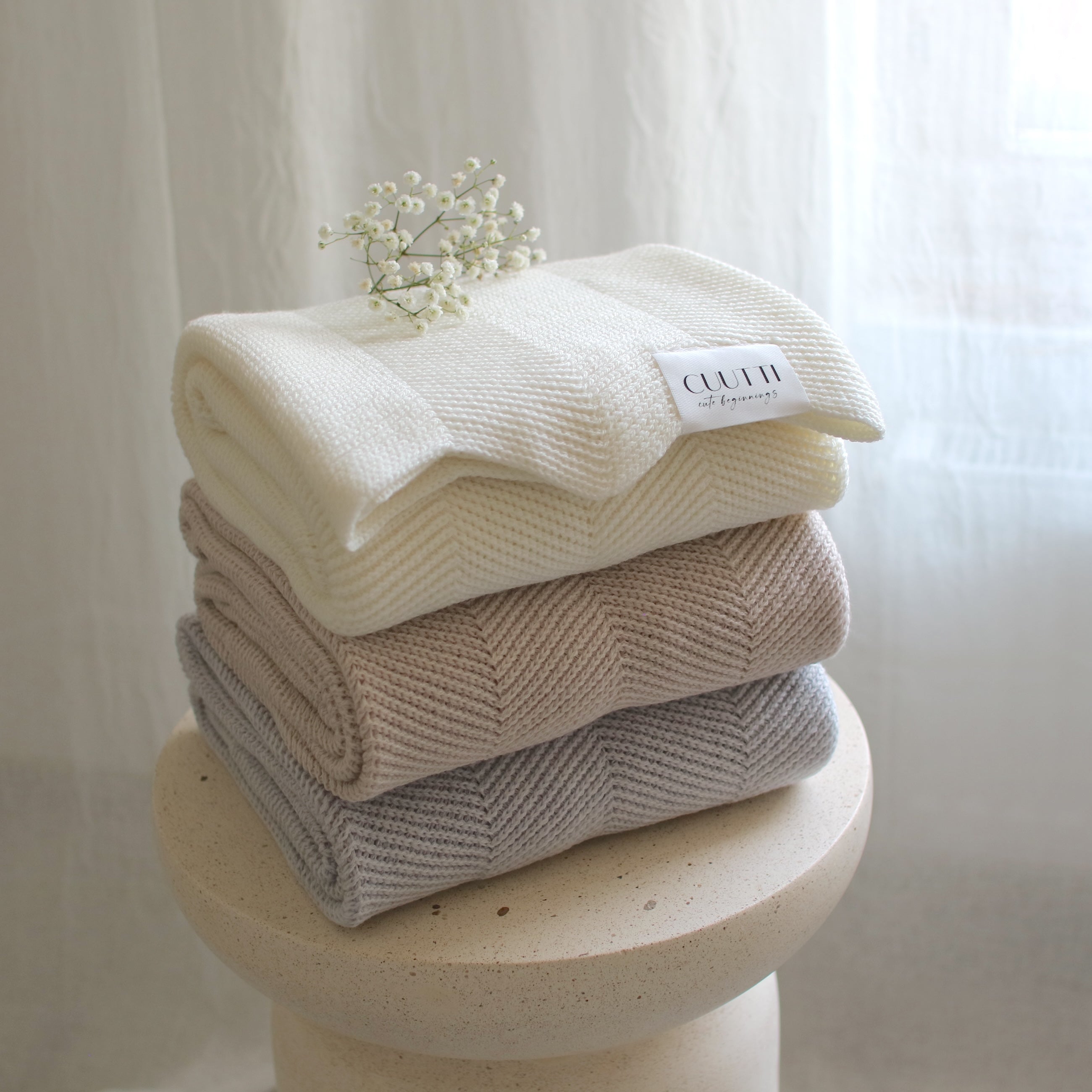 Three CUUTTI 100% merino wool Harmony blankets in ivory, beige, and cloud color neatly folded on a small table.