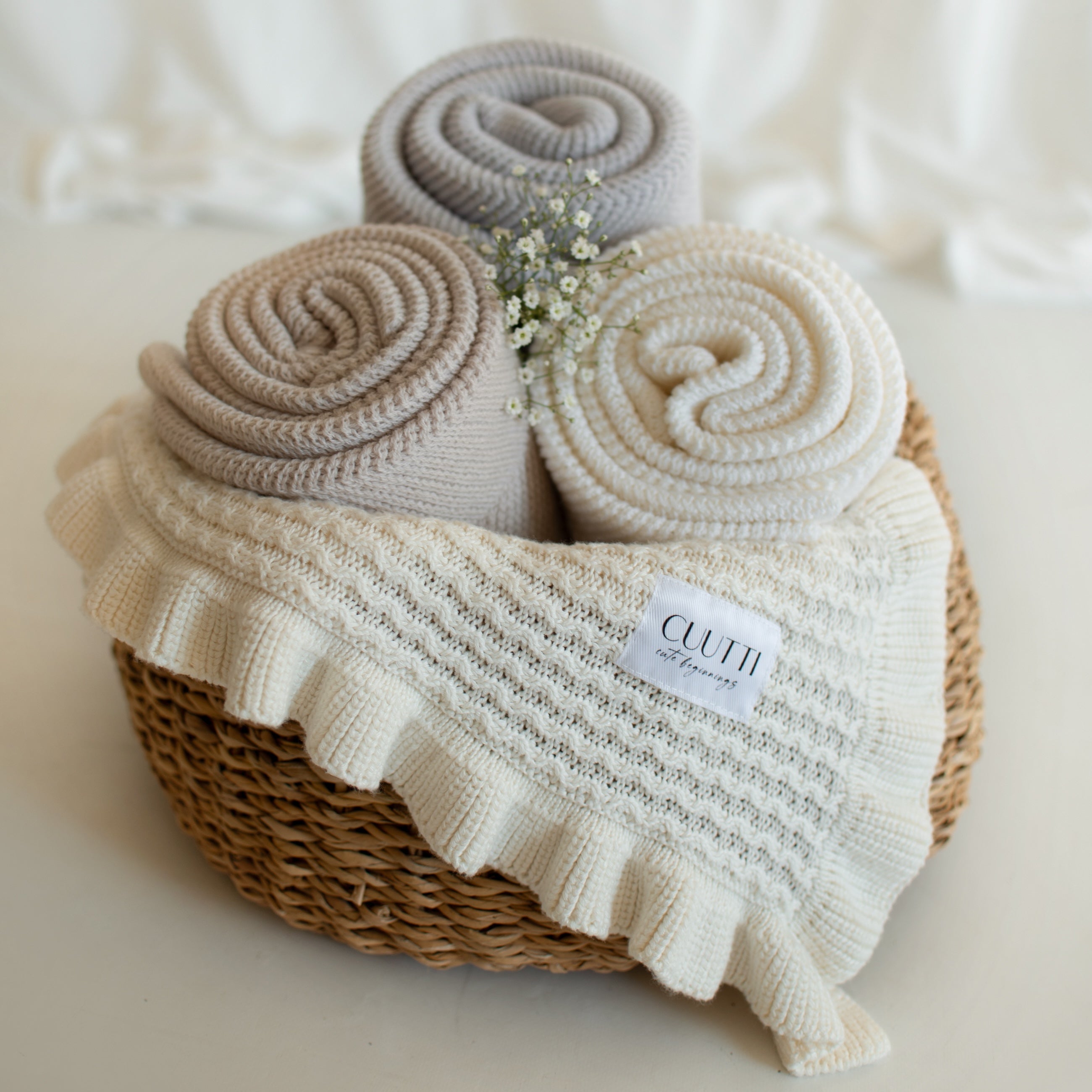 Three CUUTTI 100% merino wool Harmony blankets in ivory, beige, and cloud color neatly rolled inside a small basket.