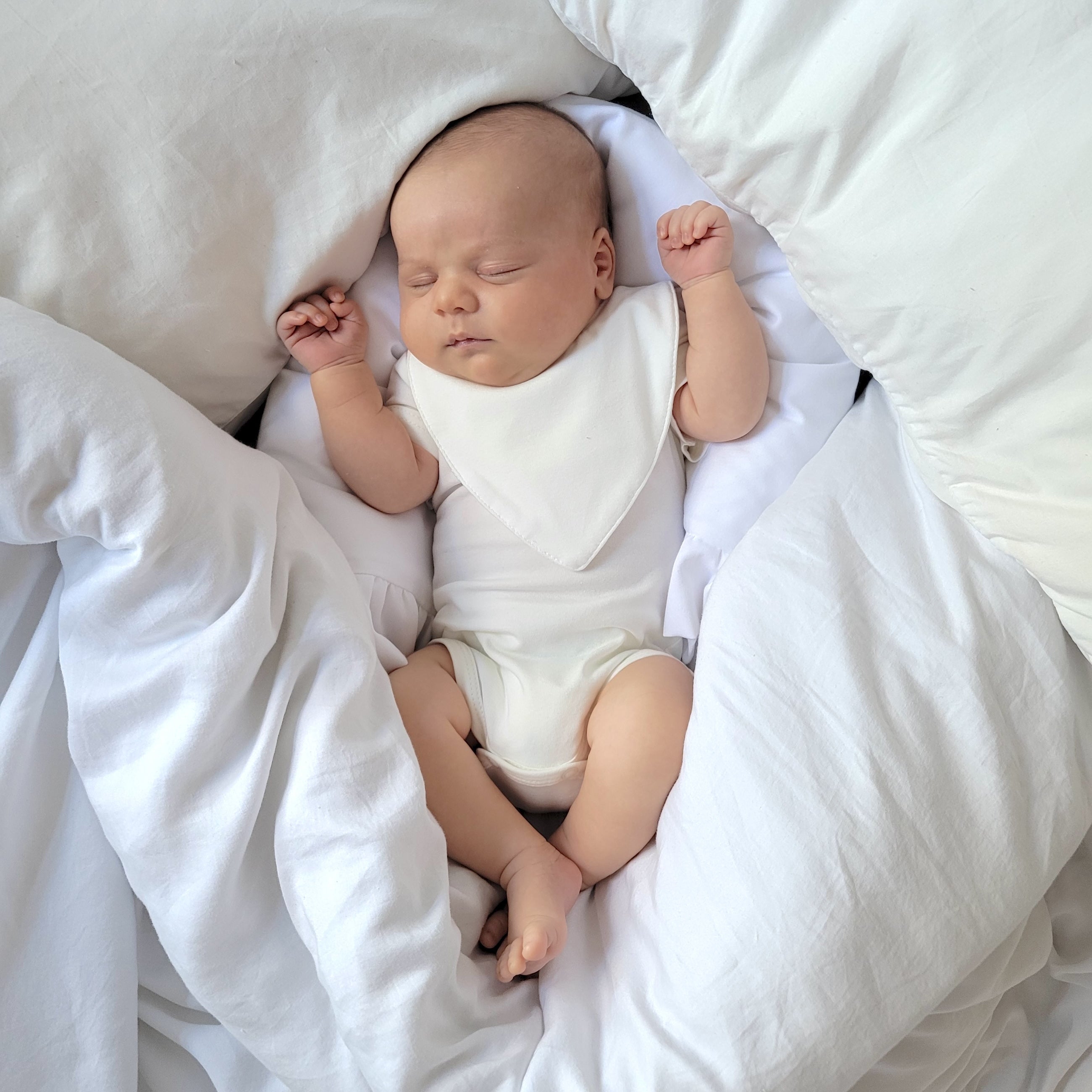 Newborn baby boy peacefully sleeping on a bed, dressed in an ivory CUUTTI short sleeve bodysuit and a matching ivory CUUTTI waterproof bib.