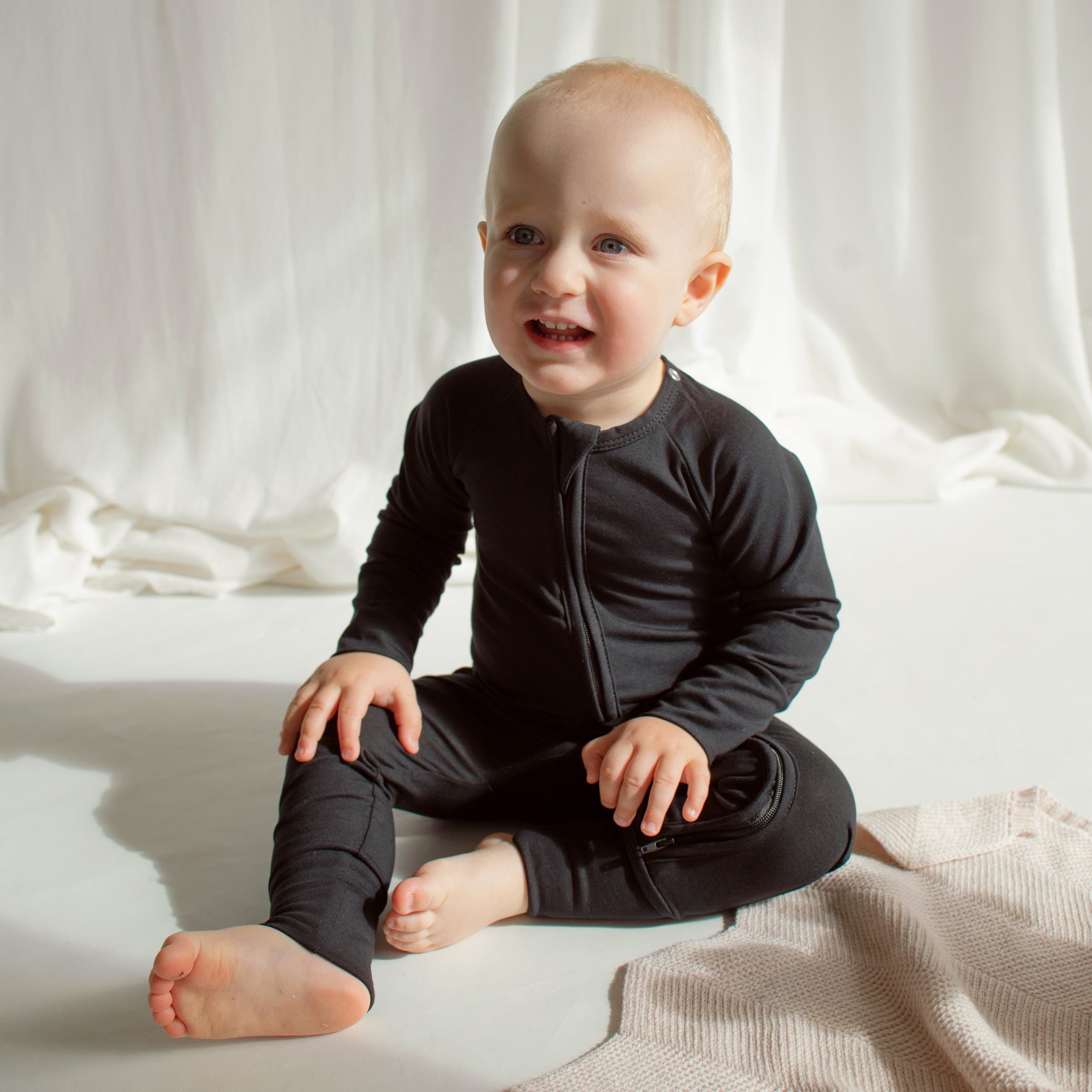 Little boy sitting on the floor in a black CUUTTI zipper onesie.