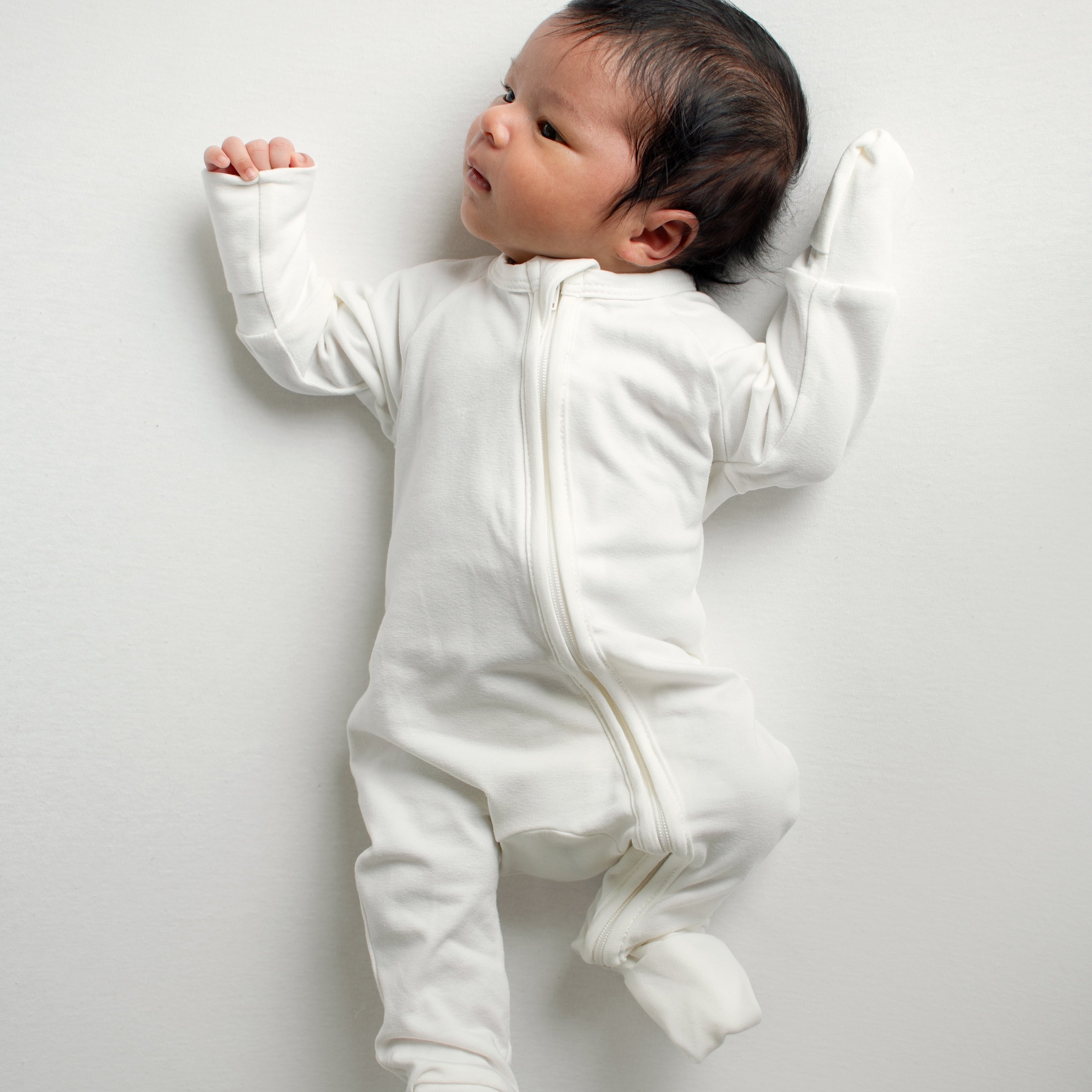 One-month-old baby boy in an ivory CUUTTI zipper onesie, left arm with a foldable hand mitten in use, right arm free to show the difference.