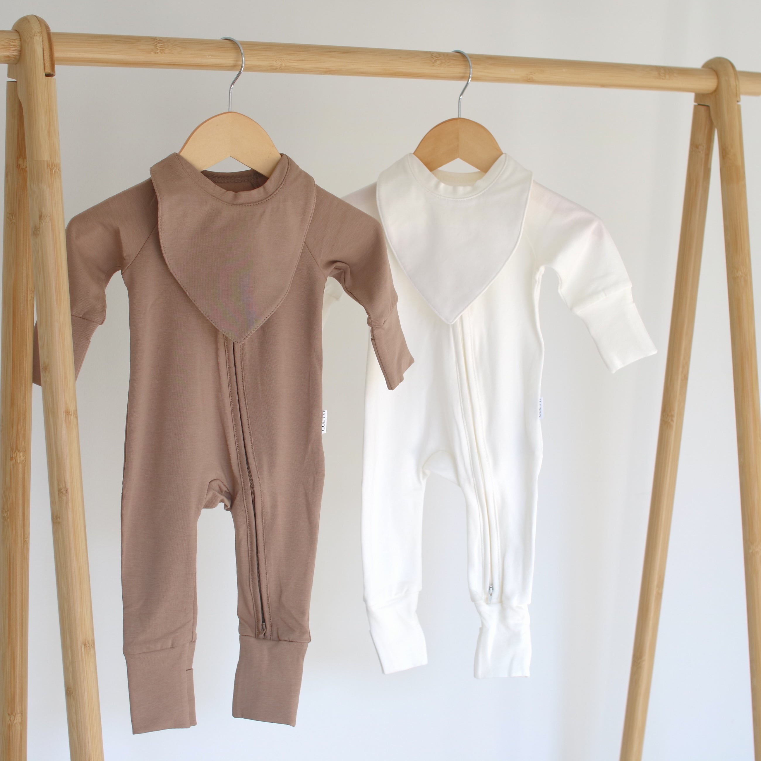 A pair of CUUTTI zipper onesies in cookie and ivory colors, each featuring a matching waterproof bib.